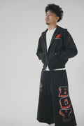 Man leaning against a wall wearing a black Basement Boy crop zip-up hoodie and matching sweatpants