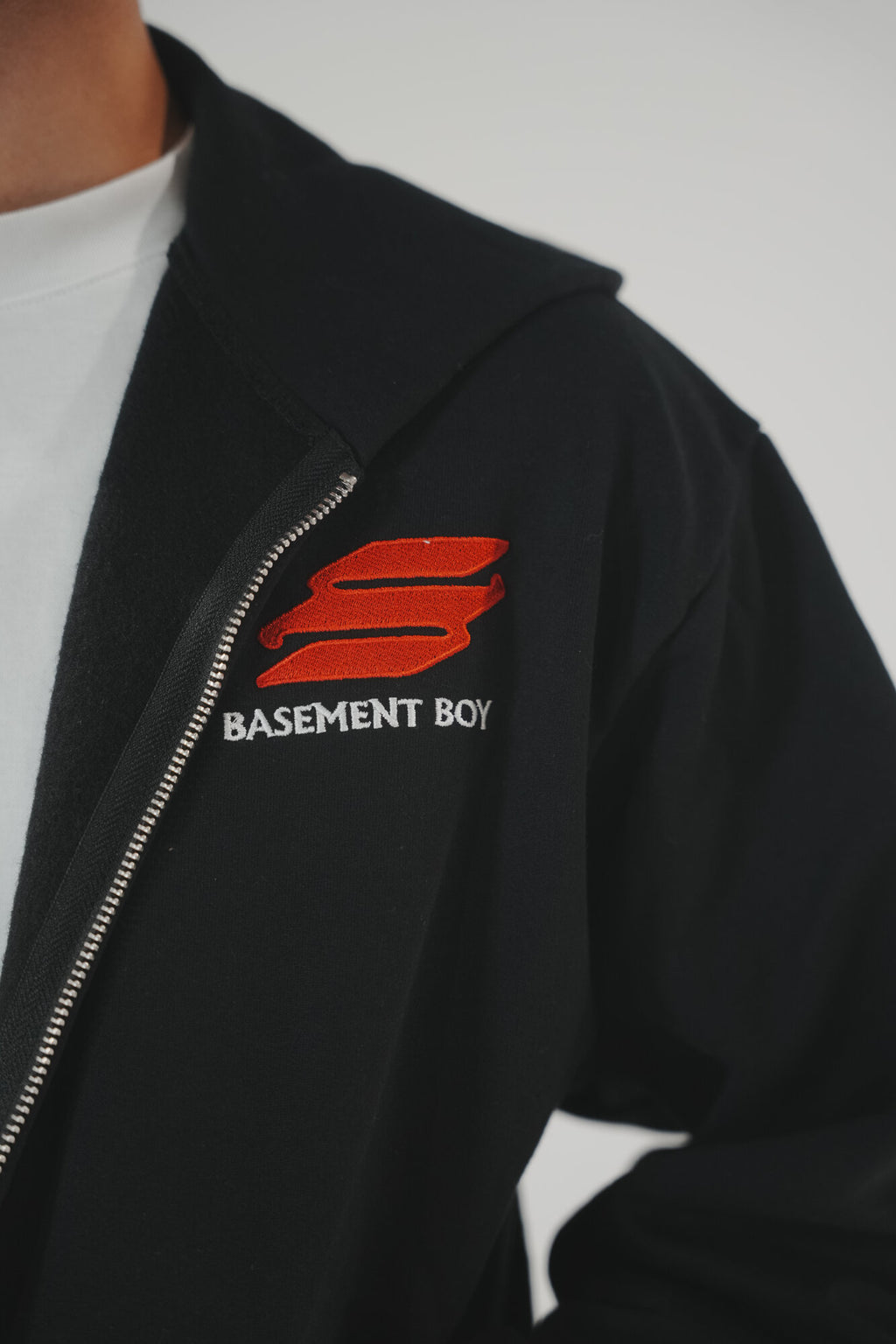 Close-up of the embroidered Basement Boy logo on a black crop zip-up hoodie